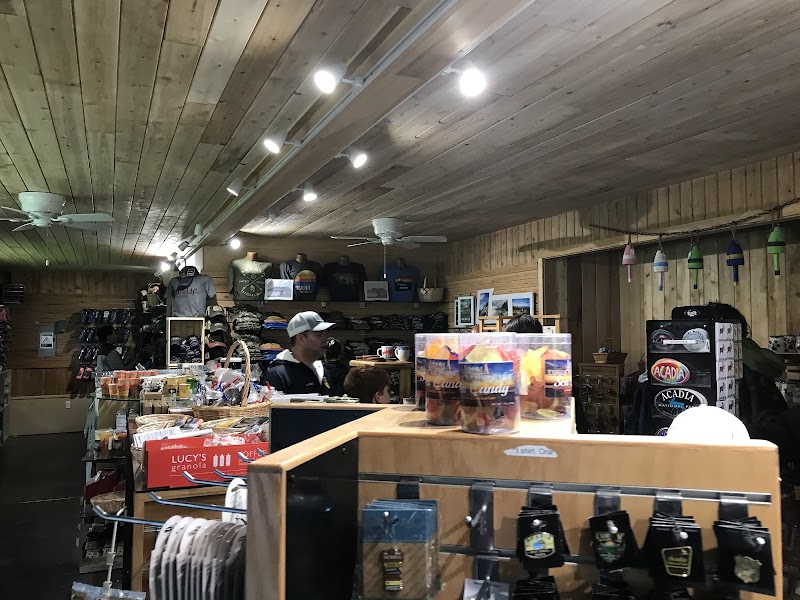 Wood-paneled gift shop inside Acadia National Park displaying t-shirts, hats, mugs, and souvenirs near a checkout.