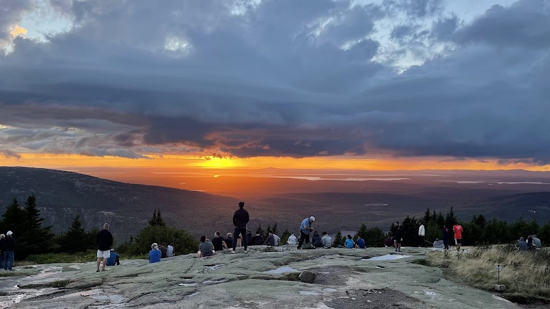 Sunset over a rocky overlook at Acadia National Park, with people seated and standing on a flat granite slab.