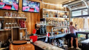 Wood-paneled bar with beer taps, glassware, and two TVs showing a car race in Arches National Park.