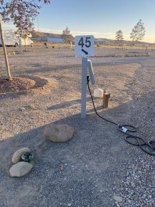 Campground at Arches National Park featuring a numbered 45 sign on a gray post, electrical hookup, gravel lot, and distant RVs.
