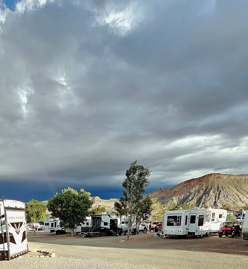 Row of RVs and campers parked among trees with desert hills and dramatic clouds at Arches National Park.