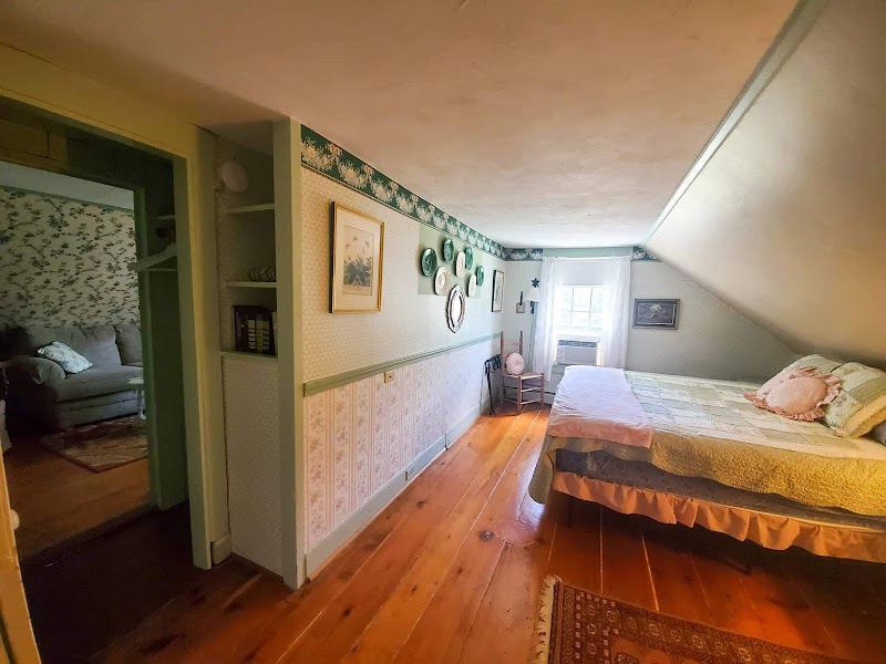 Cozy inn bedroom inside Acadia National Park with a neatly made bed, vintage wallpaper, and warm wood floors.