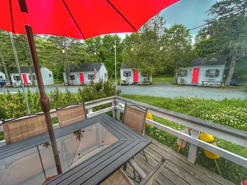 Lodge deck with a glass table and chairs overlooking a row of cabins with red doors in Acadia National Park.