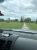 Gravel road in a grassy field near Surry in Acadia National Park, Maine, with trees and a distant shoreline under cloudy skies.