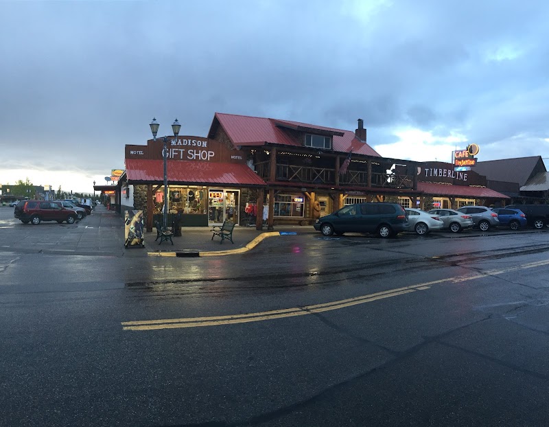 Rustic red-roofed two-story shop complex with signs, parked cars, and wet streets in Yellowstone National Park.