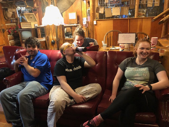 Inside a rustic gift shop in Yellowstone National Park, four friends lounge on a red leather couch, with drinks and smiles.