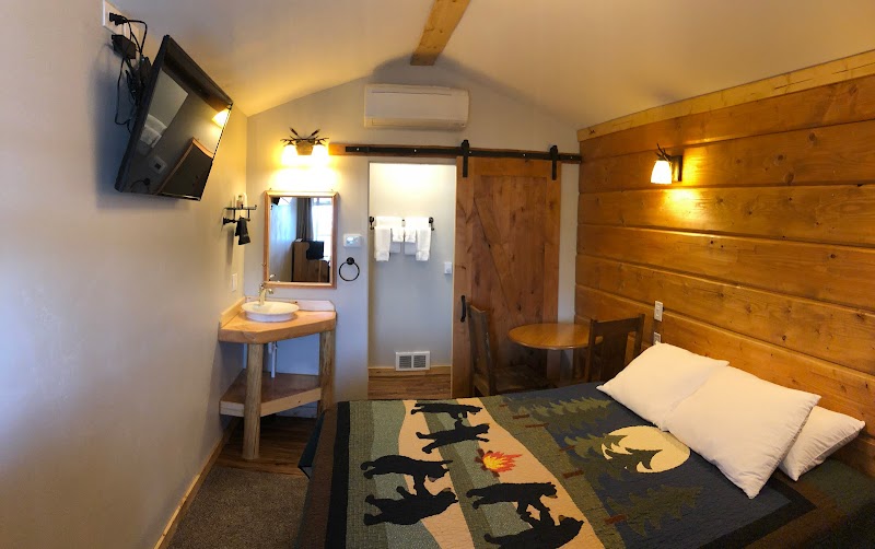 Rustic hotel room with wood walls, bed with a southwest quilt, sink vanity, TV, and a sliding barn door in Yellowstone National Park.