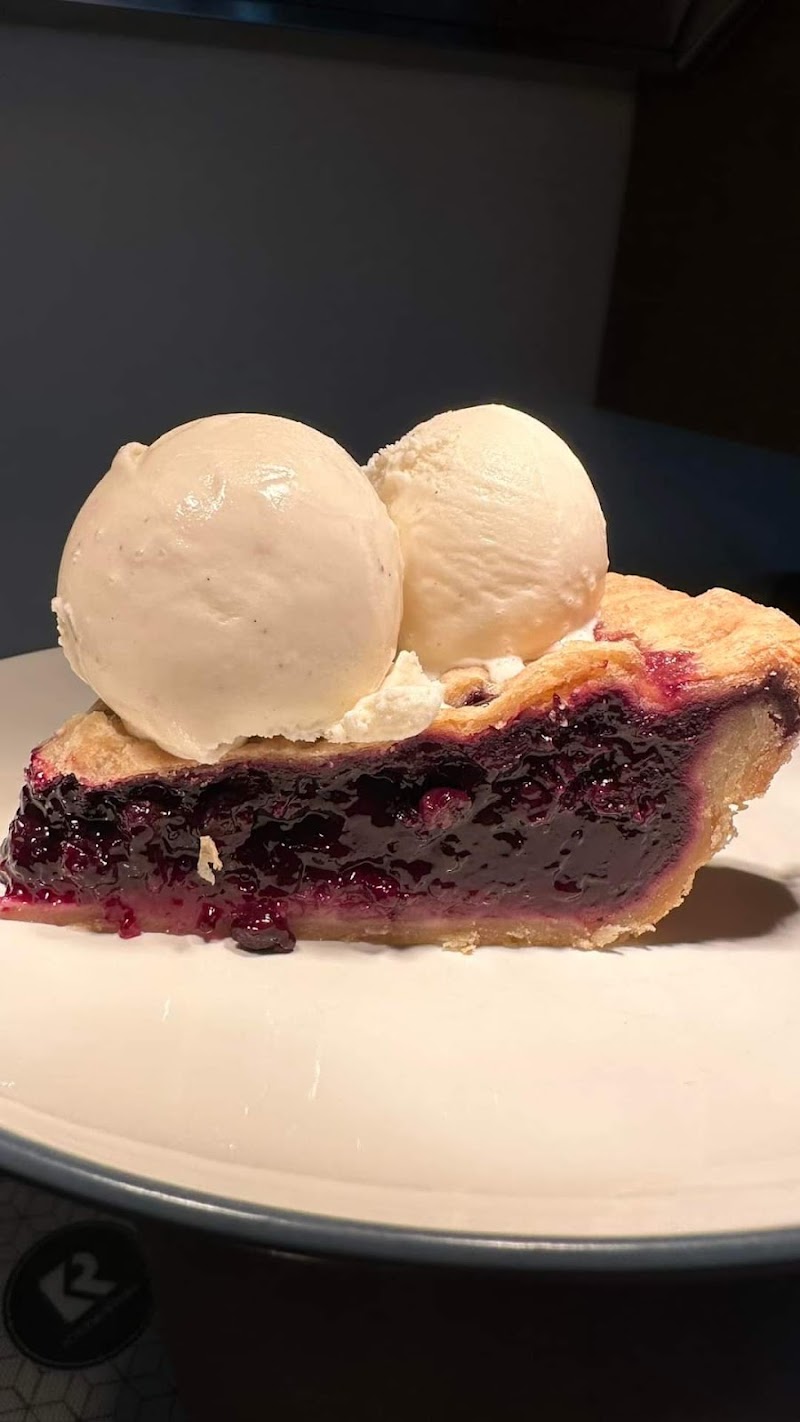 Slice of blueberry pie with juicy berry filling and two scoops of vanilla ice cream on a white plate, Acadia National Park.