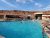 Outdoor pool at a beige desert lodge with red rock cliffs, guests swimming under a clear blue sky at Arches National Park.