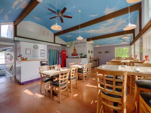 Thai restaurant interior inside Acadia National Park, featuring blue sky ceiling, wooden beams, and round dining tables.