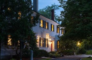 Inn-style lodging in Acadia National Park glows warmly at dusk along a tree-lined colonial façade.