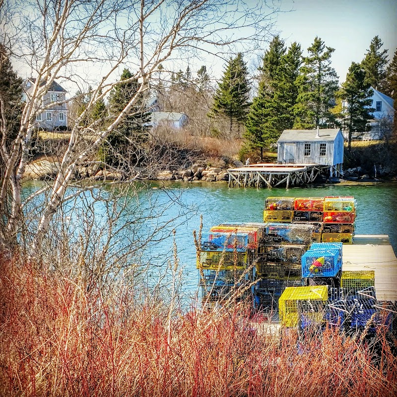 Gouldsboro waterfront at Acadia National Park shows a dock with colorful lobster crates and a small boathouse along calm blue water.