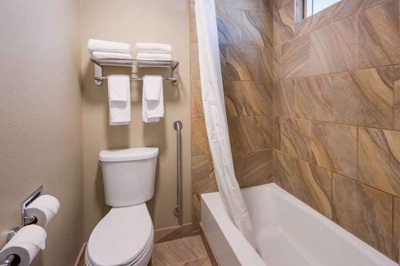 Cozy lodge bathroom with a toilet, towels on a rack, white tub and shower curtain, tan tile walls in Yellowstone National Park.