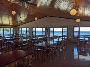 Ocean-view dining hall in Acadia National Park, with wooden ceiling, round pendant lights, and tables by the Atlantic windows.