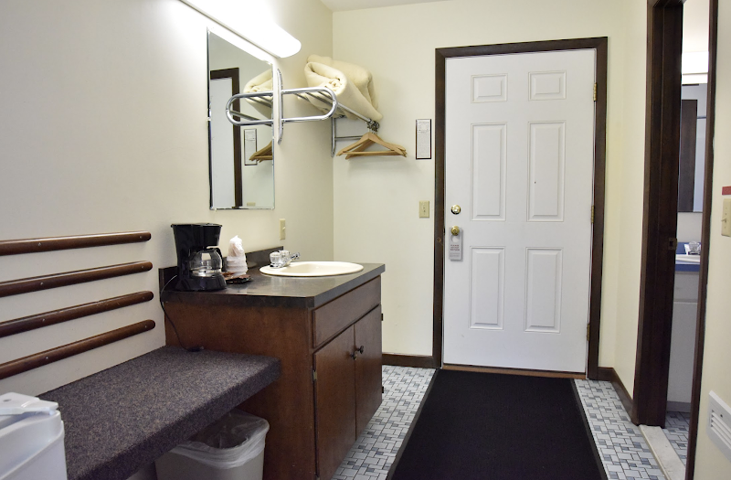 Bathroom and entry area of a guest lodging room in Acadia National Park, with a sink, coffee maker, bench seating, and a wall mirror.