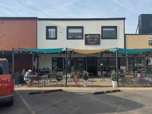 Outdoor cafe seating under teal and yellow awnings in front of a two-tone storefront, Arches National Park area.