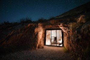 The Summit at Big Bend lodging carved into a rocky hillside with a glass-walled entrance, illuminated against a starry night sky in Big Bend National Park.