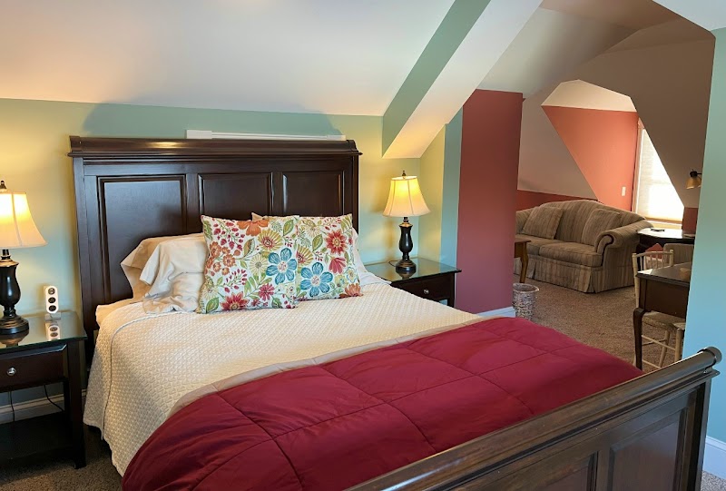 Cozy inn bedroom interior in Acadia National Park, showing a dark wood bed frame, colorful pillows, and a burgundy comforter.