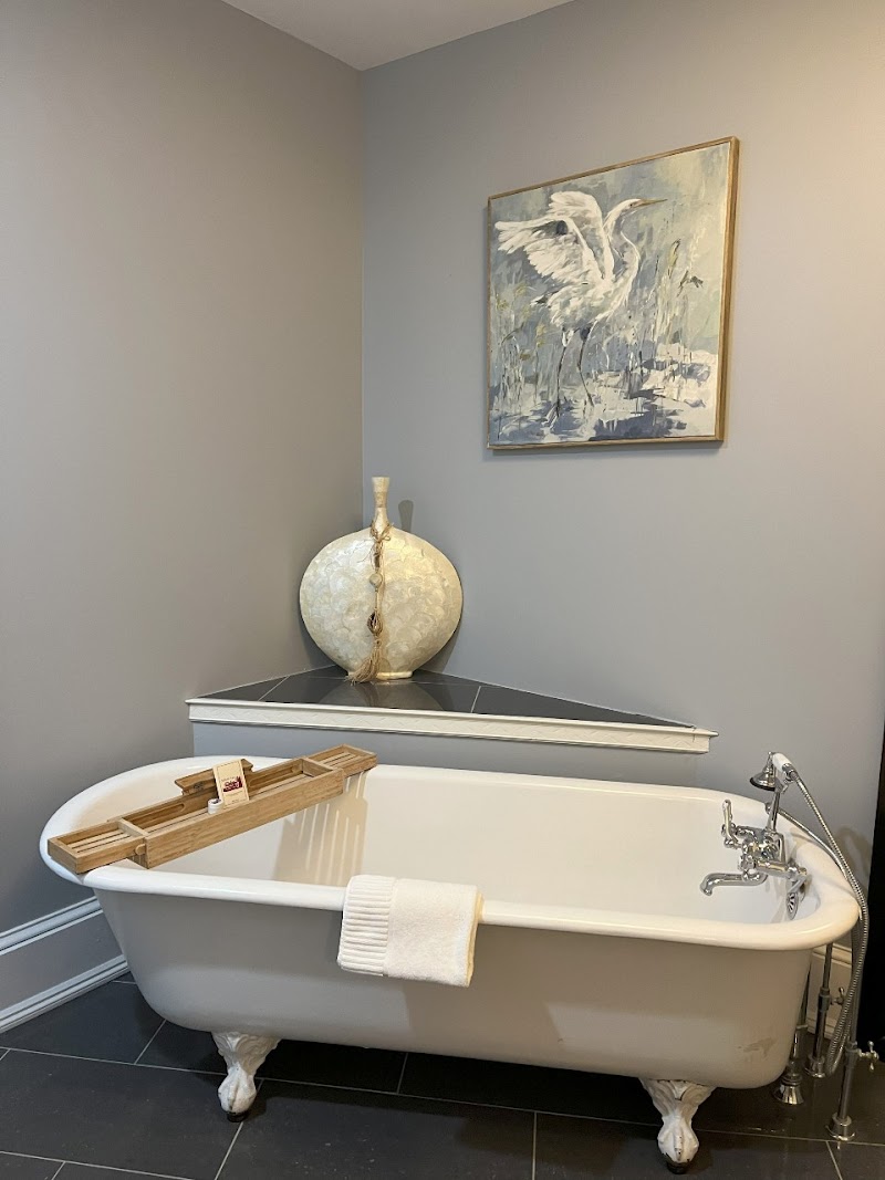 Waterfront inn bathroom with a white clawfoot tub and a framed swan painting on the wall in Acadia National Park lodging.