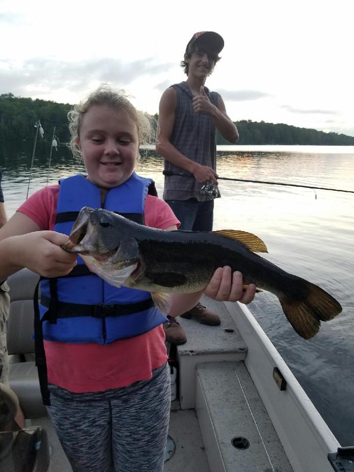 Young camper in a life jacket proudly holds a large bass aboard a boat at Balsam Cove Campground, Acadia National Park.