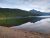 Glacier National Park: a calm lake with evergreen shoreline, pebbled beach, and mountains reflected on the glassy water.