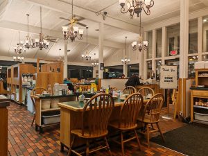 Interior of a Yellowstone National Park restaurant with wooden tables, long communal seating, and decorative chandeliers.