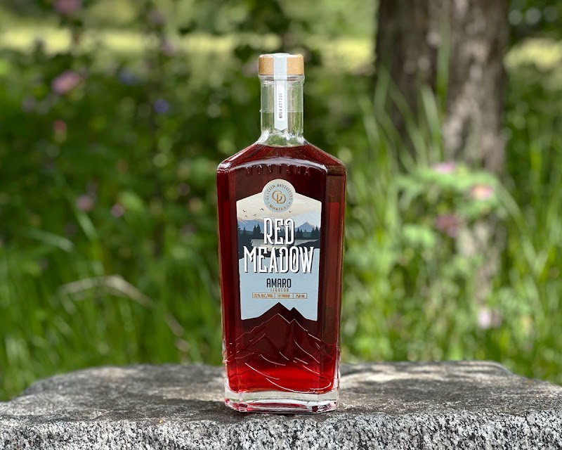 Red Meadow amaro bottle sits on a stone ledge with greenery in Glacier National Park.