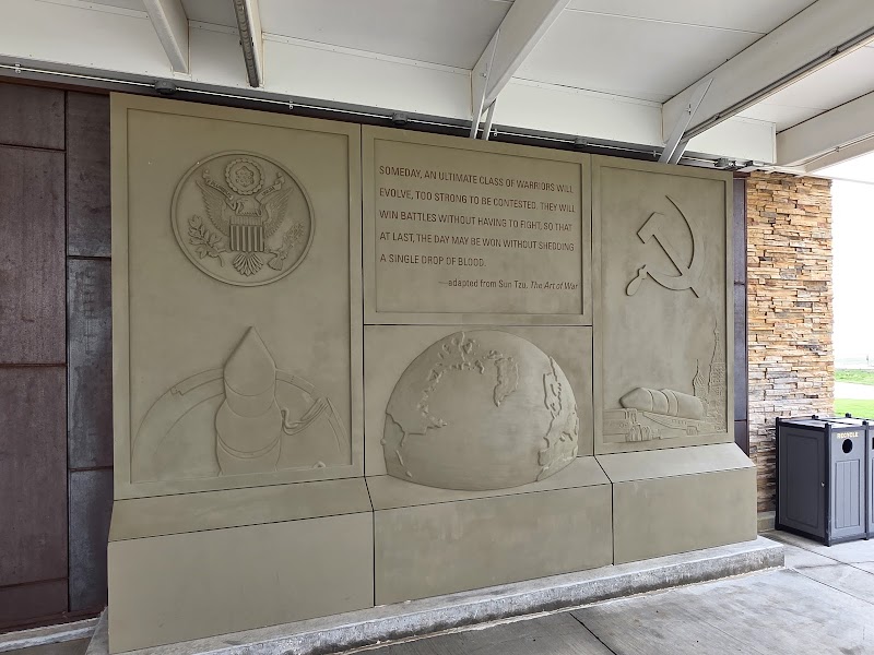 Stone relief panels at Badlands National Park Visitor Center show the U.S. seal, a globe, and a hammer‑and‑sickle motif with an inscription.
