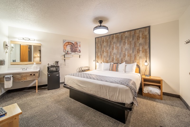 Cozy lodge room at Badlands National Park with a king bed, rustic wood headboard, two nightstands, and a small kitchenette.