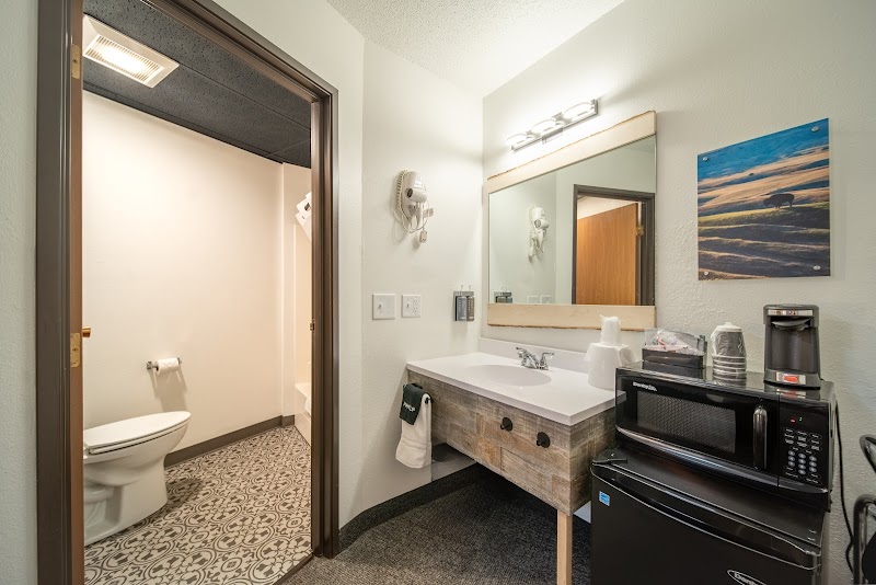 Bright hotel bathroom with wooden vanity, large mirror, coffee station, microwave and mini fridge, Badlands National Park.