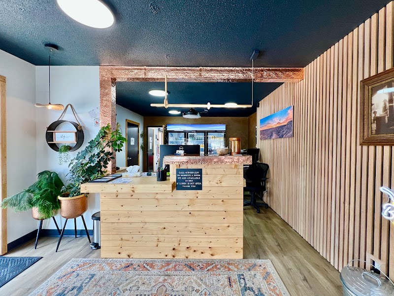 Cozy lobby with a wooden reception desk, hanging lights, potted plants, and a rustic paneled wall in Badlands National Park.