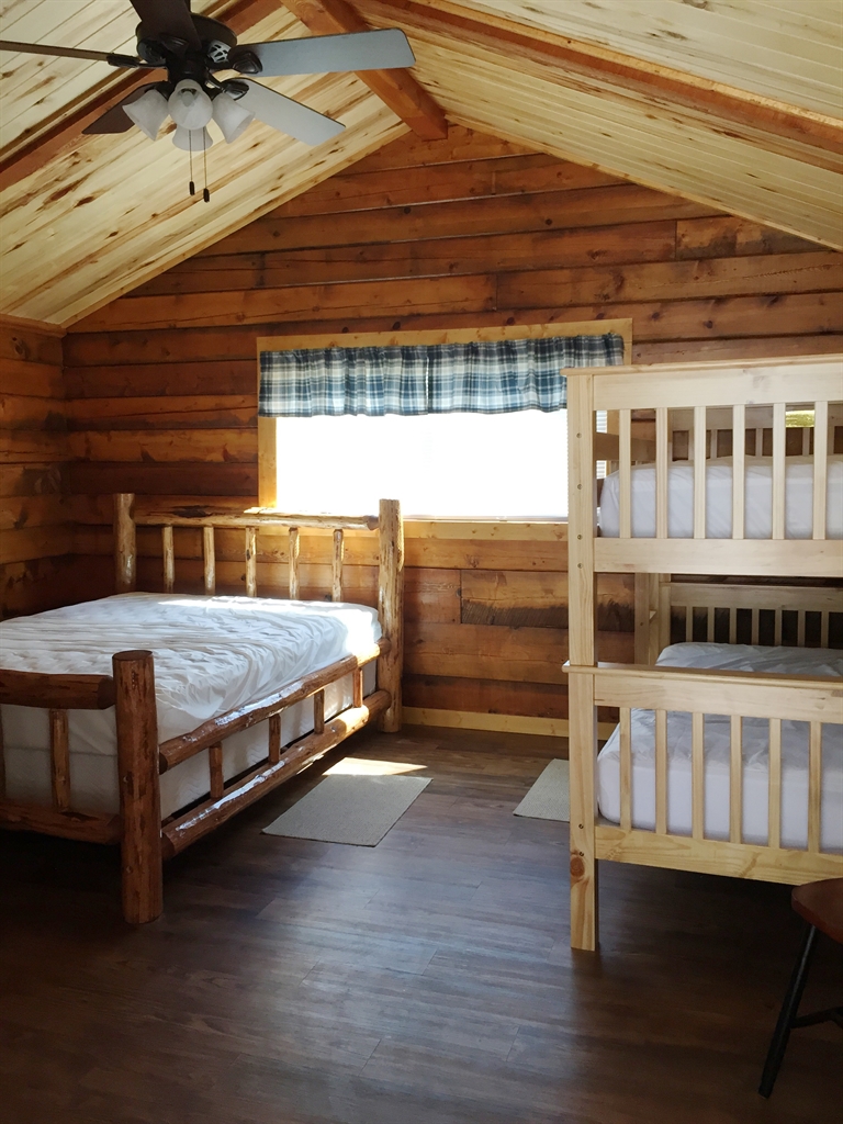 Rustic Glacier National Park cabin bedroom with a full bed and a wooden bunk bed, plaid window valance.