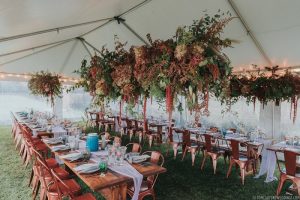 Event tent setup with long wooden tables and hanging florals in Acadia National Park.
