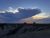 Sunset over a line of RVs parked along a ridge at a Badlands National Park campground with dramatic clouds.