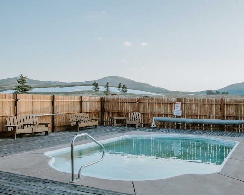 Outdoor pool on a wooden deck with a metal handrail, benches along a privacy fence, overlooking a lake and distant hills in Yellowstone National Park.