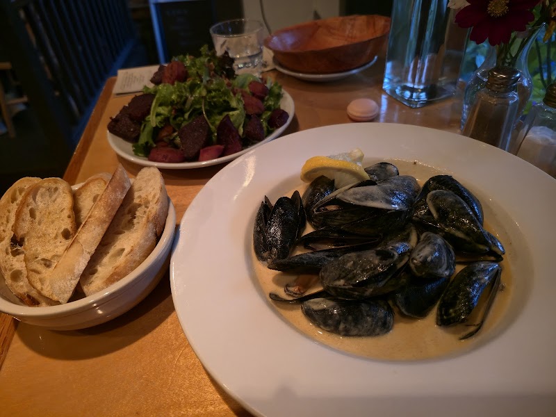 Plate of creamy mussels with lemon in Acadia National Park, with sliced baguette and a greens salad in the background.