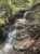 Columbia Mountain Trailhead scene in Glacier National Park shows a rocky waterfall along a forested trail.