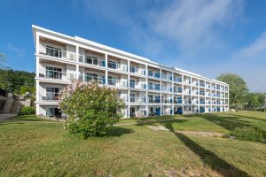 White four-story hotel with glass balconies, green lawn, and a blooming shrub in Acadia National Park.