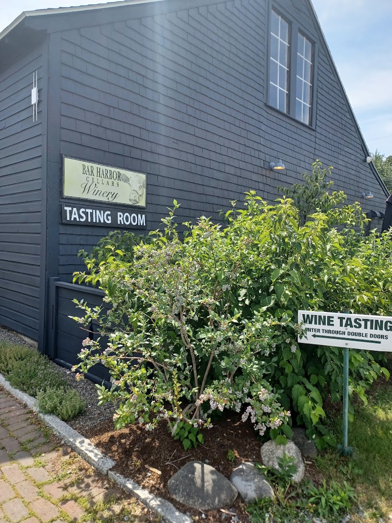 Quaint blue-tinted tasting room building in Acadia National Park, surrounded by shrubs and a garden.