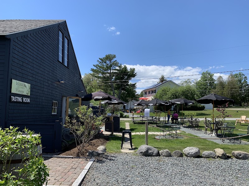 Winery tasting room at Acadia National Park’s Bar Harbor area with outdoor seating under umbrellas and a dark blue building.