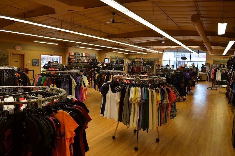 Inside a Badlands National Park gift shop, rows of clothing racks hold colorful shirts and tees under bright ceiling lights.