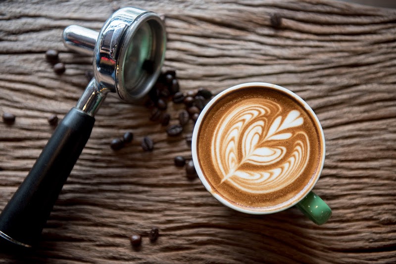 Espresso portafilter beside a cup of latte art on a rustic wooden table with scattered coffee beans, Acadia National Park.