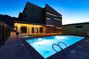 Modern hotel building beside a illuminated rectangular pool at dusk, fenced patio, Arches National Park.