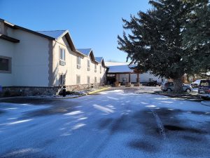Exterior view of a lodge in Yellowstone National Park with snow on the pavement and a large pine tree.