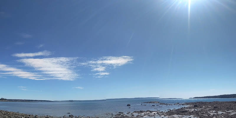 Lamoine Beach shoreline along Acadia National Park with calm bay and sunny sky today.