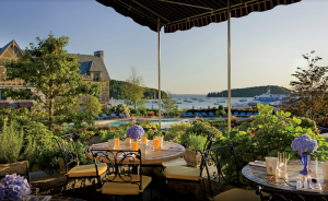 Harborside dining terrace overlooking the harbor and boats at Acadia National Park, with striped awning and floral planters.