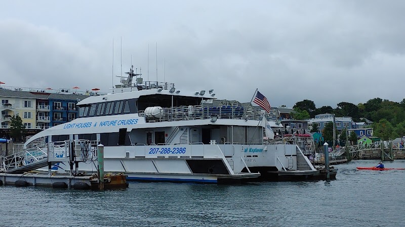 White tour boat docked at a marina in Bar Harbor, Acadia National Park, under a gray sky beside waterfront buildings.