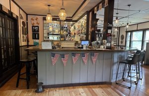 Cozy bar interior with a long counter, hanging lanterns, bottle shelves, and US bunting in Acadia National Park.