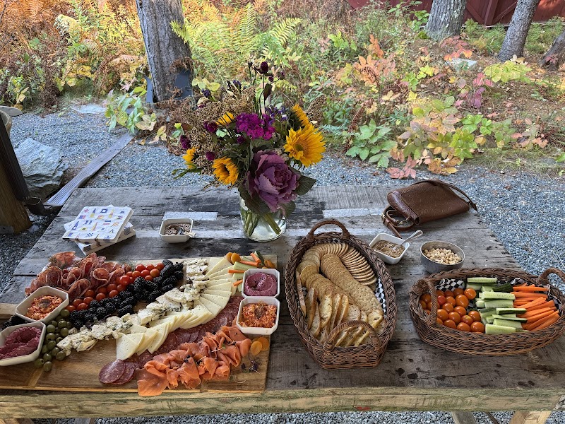 Outdoor charcuterie spread on a rustic wooden table with fall foliage around, in Acadia National Park.