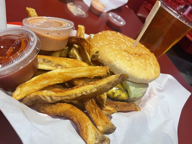 Golden french fries spill over a tray next to a cheeseburger with sesame bun, two sauces, and a frosty drink on a red table at Arches National Park.